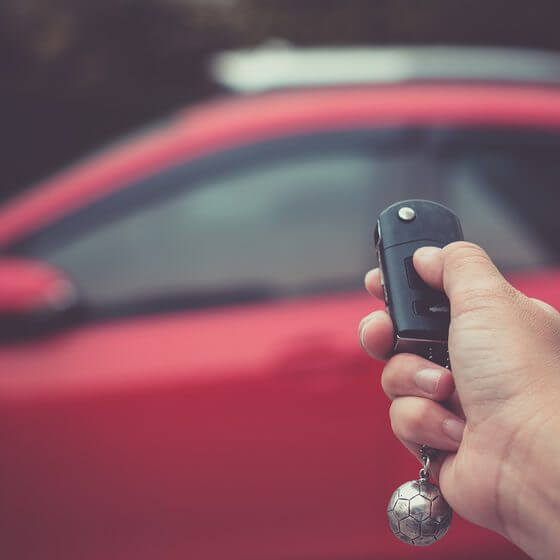 red car in background with a person's hand using key to lock